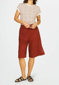 Haut blanc avec un motif de feuille rouge, associé à un short ample de longueur genoux en marron. Porté avec des sandales noires au design texturé.