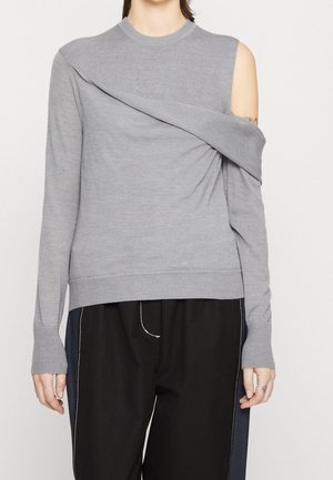 Maglione grigio a maniche lunghe in maglia con design asimmetrico, spalla scoperta e texture a costine. Abbinato a pantaloni neri.
