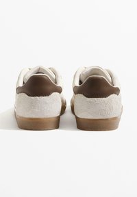 Valkoiset ja ruskeat tennarit, joissa on teksturoitu mokkanahkainen kantaosa, sileä nahkainen yläosa ja kumipohja sekä pehmustettu nilkkakaulus.