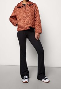 Rdzawobrązowa pikowana krótka kurtka z kołnierzem, zapinana na guziki i posiadająca kieszenie, zestawiona z czarnymi rozszerzanymi spodniami i czarno-białymi sportowymi butami.