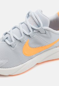 Chaussure de sport bleu clair avec une texture rayée, dotée d'un swoosh Nike orange et d'accents assortis, bout rond et semelle rembourrée.