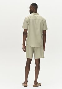 Maglietta verde chiaro a maniche corte e pantaloni corti in tessuto testurizzato. Vestibilità rilassata, orlo della maglietta curvo e design informale. Indossato con sandali piatti.