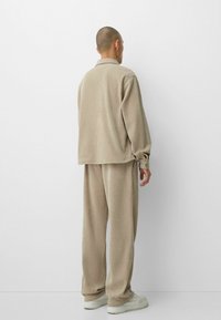 Conjunto de loungewear de canalé en color beige que incluye una camiseta de manga larga y pantalones a juego, fabricado en un material suave, con un corte relajado y una cintura elástica.