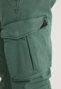 Gröna bomullscargobyxor med en ficka med lock, detaljerad sömnad och en liten svart logotyp. Har en avslappnad passform och en jämn textur.