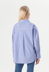 Camicia a righe blu chiaro con maniche lunghe, caratterizzata da righe verticali e polsini con bottoni. Il dettaglio della spalla posteriore aggiunge struttura e texture.