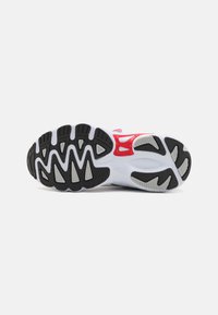 Suela de zapatilla deportiva en goma negra con secciones en blanco y gris. Presenta un patrón texturizado para mayor agarre y acentos rojos en el diseño.