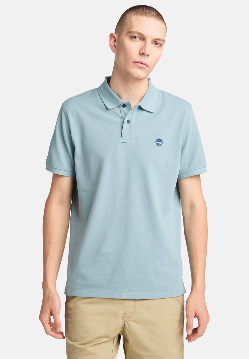 Ljust blå polo skjorta i bomull med klassisk krage, tvåknappslåsning och en liten logotyp på vänster bröst. Korta ärmar.