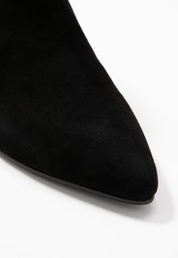 Czarne zamszowe botki za kostkę z ostrym noskiem i gładką teksturą, charakteryzujące się elegancką sylwetką i minimalistycznym designem.