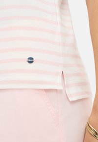 Stribet polo t-shirt i hvid og lys pink, med en sidesplit og et lille metal-logo ved kanten. Glat tekstur.