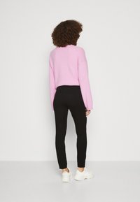 Pink knitted sweater with a relaxed fit, paired with black fitted leggings and white sneakers. Smooth texture and simple design.