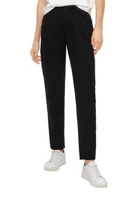 Zwarte taps toelopende broek gemaakt van lichtgewicht stof met zijzakken, met een middenhoogte taille en gedragen met witte sneakers.
