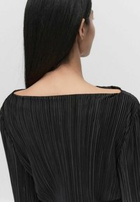 Sort plisseret top med bred, off-the-shoulder halsudskæring, der fremhæver lodrette folder og en glat overflade. Bagsiden har et rent design.