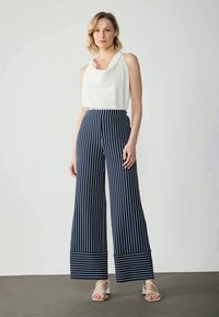 Calças largas listradas azul-marinho com uma cintura alta, combinadas com uma blusa sem mangas branca. As riscas têm um detalhe horizontal nas bainhas.