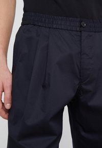 Námořnické modré kalhoty s volným střihem vyrobené z lehkého materiálu, s elastickým pasem, sklady a jedním knoflíkem na zapínání.