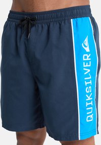 Ναυτικά σορτς για κολύμβηση με ελαστική μέση και κορδόνι. Διαθέτουν μπλε πλαϊνή λωρίδα με το κείμενο "QUIKSILVER" και λευκές λεπτομέρειες. Ομαλή υφή.