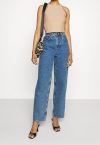 Top senza maniche color tan, jeans in denim blu a vita alta e sandali neri con tacco. Borsa con stampa animale e tracolla.