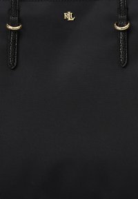 Svart tote-väska i texturerat material med dubbla svarta handtag. Har en liten guldfärgad logotyp och metallaccenter nära handtagen.