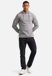 Grijze hoodie met ribbelstructuur, trekkoorden en logo. Gecombineerd met zwarte jeans en witte sneakers voor een casual look.
