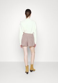 Witte geribbelde trui gecombineerd met bruine geruite shorts, met een hoge taille en achterzakken, aangevuld met gele blokhakken laarzen.