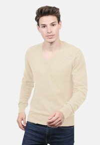 Pull à col en V beige en tricot doux et léger. Présente des manches longues et des poignets côtelés. Assorti à un jean en denim foncé.