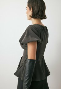 Top peplum grigio con maniche a sbuffo e corpetto aderente, tessuto texturizzato, dettaglio con zip sulla schiena. Abbinato a guanti lunghi in pelle nera.