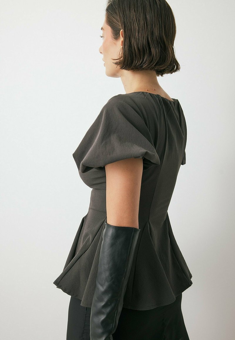 Top peplum grigio con maniche a sbuffo e corpetto aderente, tessuto texturizzato, dettaglio con zip sulla schiena. Abbinato a guanti lunghi in pelle nera.