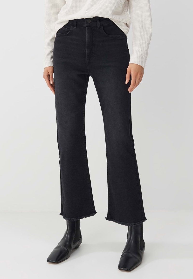 Black high-waisted flared jeans made from denim, featuring a frayed hem. Worn with black ankle boots. Smooth texture, classic five-pocket design.