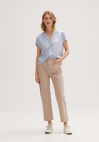 Blusa azzurro chiaro a maniche corte con scollatura a V, abbinata a pantaloni beige a gamba dritta. Le sneakers bianche completano l'outfit.