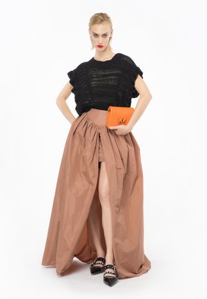 Top corto nero in maglia, gonna marrone a vita alta con spacco frontale, abbinata a una pochette arancione e scarpe con tacco nere con borchie.