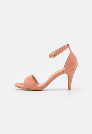 Rosa ruskinds sandal med hæl og ankelrem. Åben tå, slank 5 cm hæl og glat tekstur. Spænde til justering.