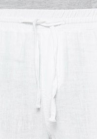 Gros plan sur la ceinture d'un pantalon en lin blanc présentant une bande élastique et un cordon de serrage noué au centre devant.