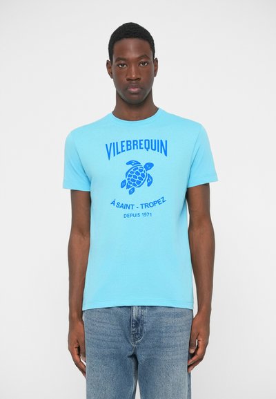 Ανοιχτό μπλε βαμβακερό t-shirt με γραφικό μιας μπλε χελώνας και κείμενο που γράφει "VILEBREQUIN A SAINT-TROPEZ DEPUIS 1971." Κλασική εφαρμογή, στρογγυλή λαιμόκοψη.