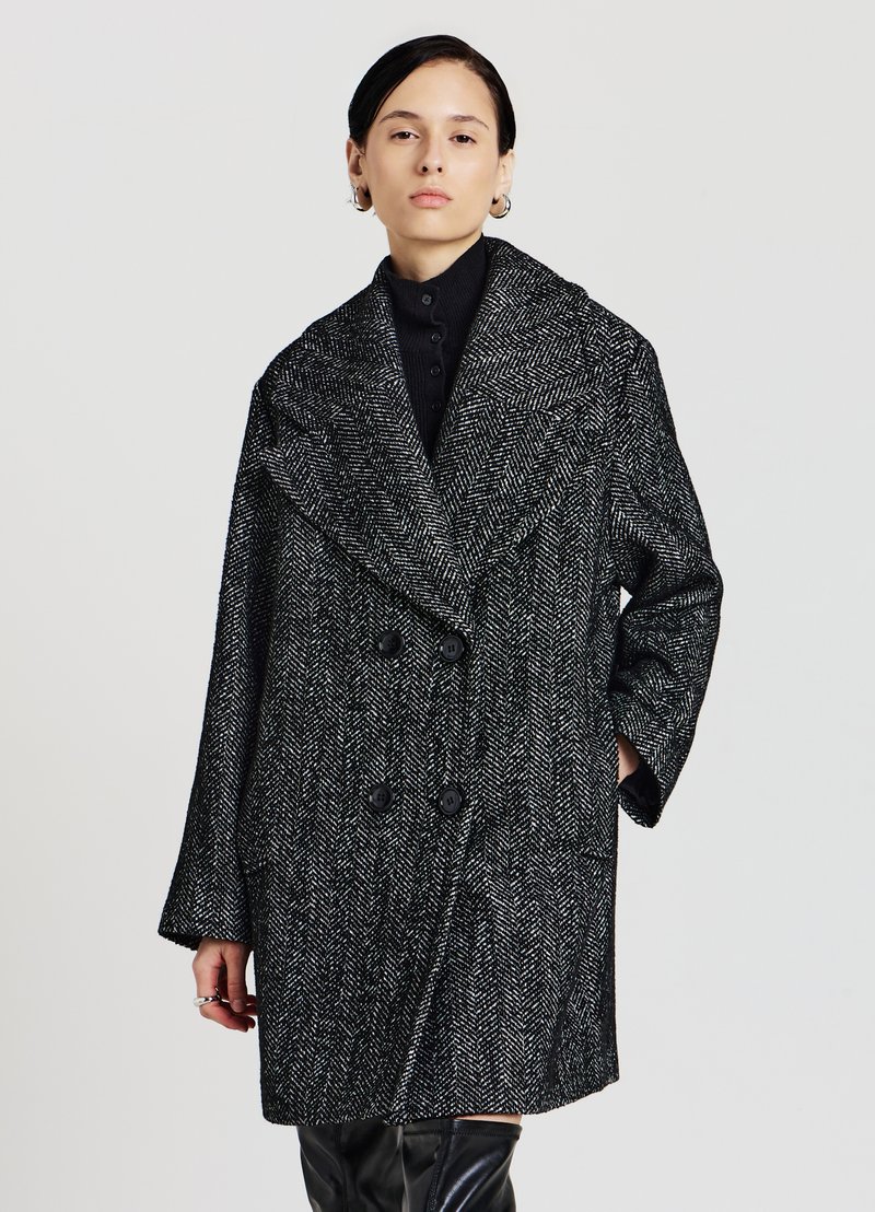 Cappotto a doppio petto in zigzag bianco e nero. Presenta ampi revers, due bottoni frontali e maniche oversize con una finitura testurizzata.