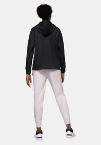 Sweatshirt à capuche noire avec une coupe ample, associé à un pantalon de jogging gris clair fuselé, complété par des baskets blanches. Texture de tissu lisse.