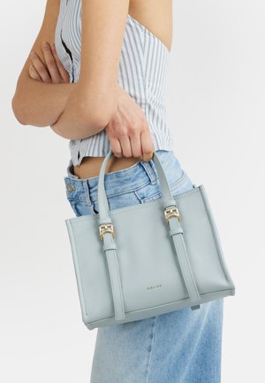 Persona con maglietta a righe e jeans, che tiene al fianco una borsa strutturata azzurro chiaro con fibbie dorate.