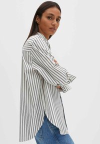 Weißes und marineblau gestreiftes Hemd mit Knopfleiste am Kragen, langen Ärmeln und seitlichen Schlitzen, getragen über blauen Jeans. Glatte Textur. Lässiger Stil.