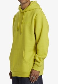 Limegrön hoodie i mjukt tyg med kängurufickor, dragsko på huvan och präglad logotyp på bröstet. Slät textur.