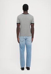 Siva majica s kratkimi rokavi in črnimi robovi, kombinirana s svetlo modrimi ravnimi kavbojkami in črnimi čevlji. Enostaven dizajn, bombažni material.