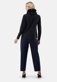 Black shirt with a ruffled collar, paired with navy trousers. The shirt features a tailored fit and long sleeves with buttoned cuffs.