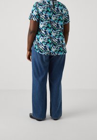 Haut à manches courtes multicolore dans un motif abstrait bleu, vert et noir ; associé à un jean en denim ample et des chaussures noires.