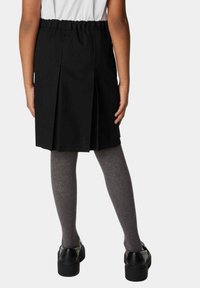 Gonna nera plissettata con vita elastica, abbinata a collant grigi e scarpe nere. Tessuto liscio con un design pulito e sartoriale.