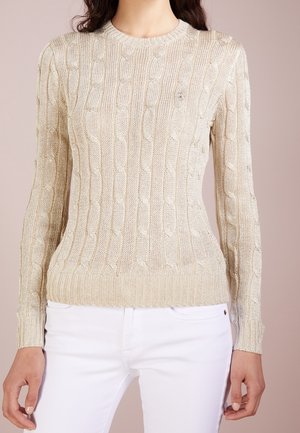 Suéter beige de punto con mangas largas, combinado con pantalones blancos, mostrado en torso y brazos sobre fondo neutro.