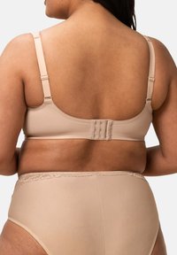 Béžová podprsenka s nastavitelnými ramínky, hladkým texturovaným materiálem a zapínáním na háček a oko. Vysoké nahé kalhotky s krajkovým lemem.