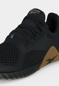 Μαύρο αθλητικό παπούτσι Reebok με άνω μέρος από δίχτυ, μαύρα κορδόνια και ταμπά σόλα με το λογότυπο της Reebok.