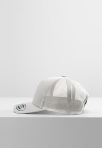 Hallja hall, millel on tahke esipaneel ja võrkkangas taga. Omab lame äärt ja nööp sulgemist. Küljel on logopatch.