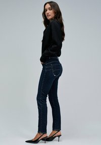 Jeans skinny de mezclilla azul oscuro con cintura alta, con bolsillos traseros y costuras mínimas. Combinados con tacones negros de punta afilada.