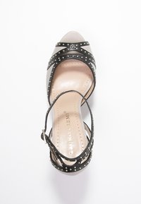 Czarna i srebrna sandałka na wysokim obcasie z paskami ozdobionymi ćwiekami, otwartym palcem oraz teksturowaną wkładką i regulowanym paskiem na kostce.