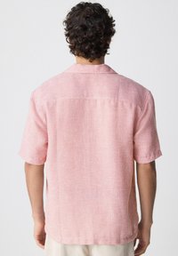 Camisa de mangas cortas en rosa claro con un patrón texturizado. Cuenta con un cuello tipo camp y un dobladillo recto, fabricada con un tejido transpirable.
