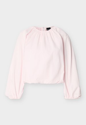 Blouse longue à manches longues de couleur rose clair avec encolure froncée, poignets élastiques, ourlet raccourci et fermeture éclair dans le dos.