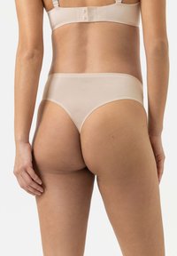 Beige nahtlose Tanga-Unterwäsche aus glattem Material, mit minimaler Abdeckung und einem elastischen Bund für einen sicheren Sitz.